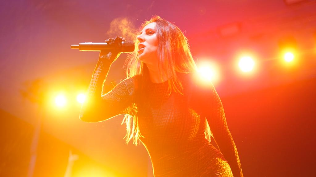 Mala Rodriguez cantando sobre un fondo alumbrado con luz cálida.